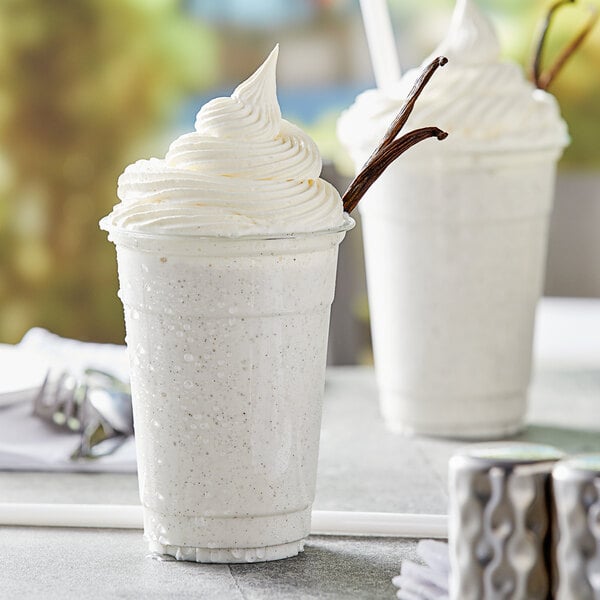 A white drink made with Capora Vanilla Bean Frappe Base Mix topped with whipped cream in a plastic cup.