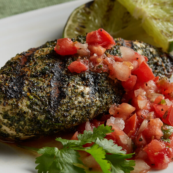 A plate of grilled chicken with salsa and lime, garnished with a slice of lime.