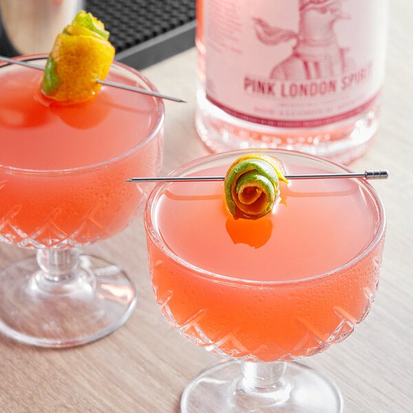 A bottle of Lyre's Pink London Spirit with two glasses of pink liquid with lemon garnish.