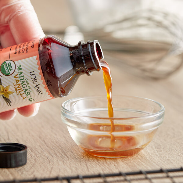 A hand pouring LorAnn Oils Organic Madagascar Vanilla Extract from a bottle into a glass bowl.