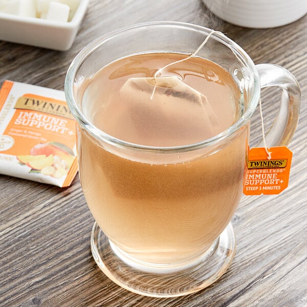 A glass mug of Twinings Immune Support+ Ginger & Mango Green Tea with a tea bag in it.