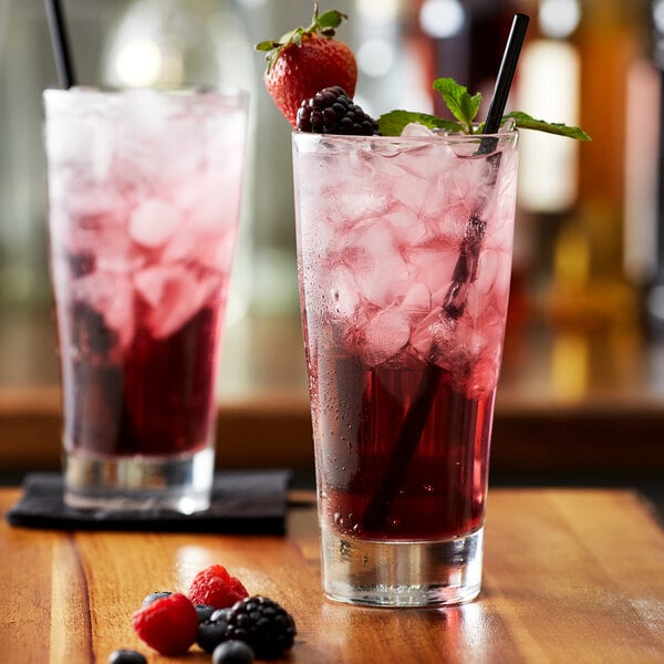 Two glasses of Monin wildberry drinks with ice and berries on a table.