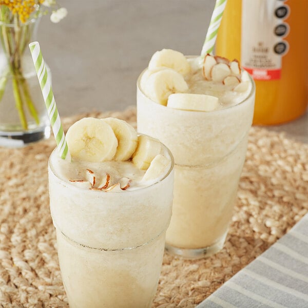 Two glasses of milkshakes with bananas and straws on top of a white background.
