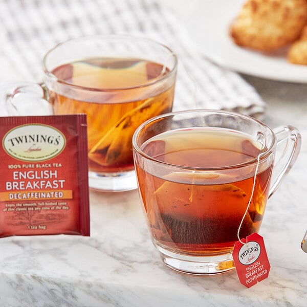 A glass cup of Twinings English Breakfast Decaffeinated tea with a tea bag next to two cups of tea.