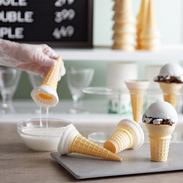 A hand dipping a waffle cone in white chocolate.