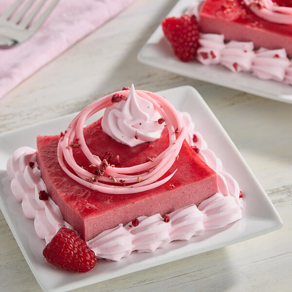 A square pink dessert with whipped cream and raspberries on a plate.
