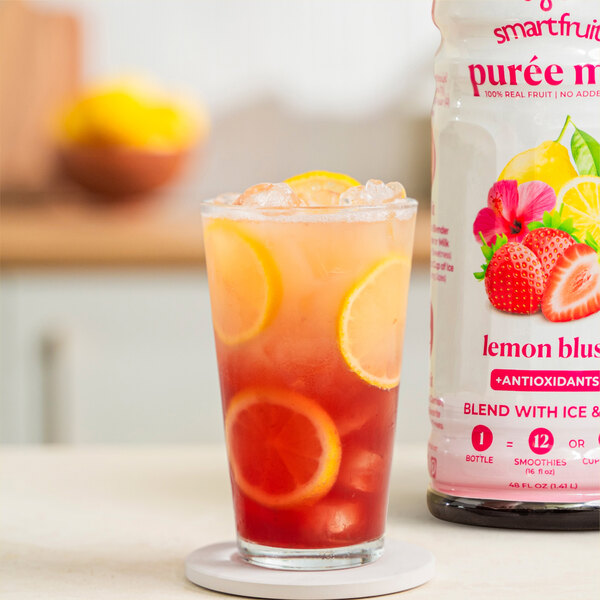 A glass of red and yellow Smartfruit Lemon Blush puree next to a white bottle.