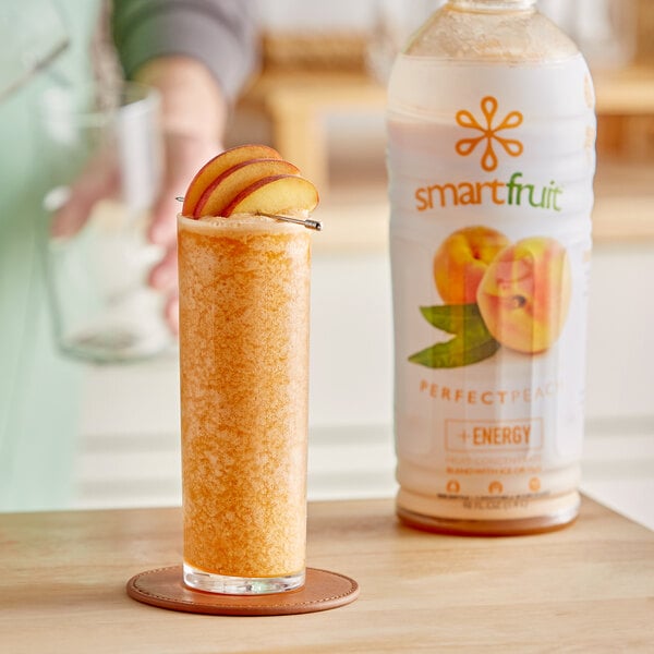 A bottle of Smartfruit Perfect Peach puree next to a glass of peach juice on a table.