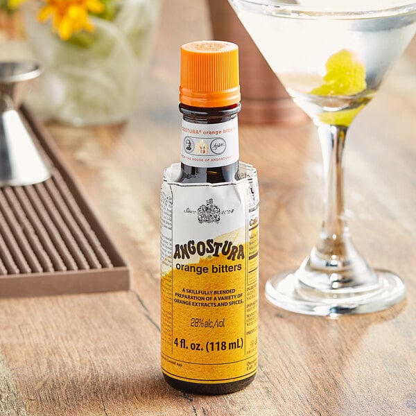 A martini glass filled with a clear cocktail next to a bottle of Angostura Orange Bitters.