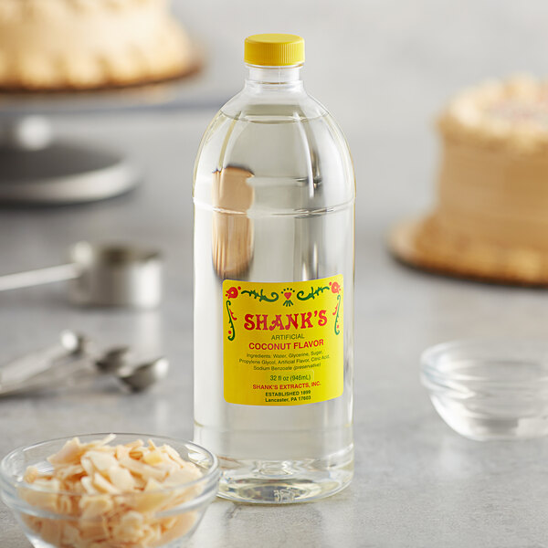 A close-up of a bottle of Shank's Imitation Coconut on a table next to a bowl of coconut flakes.