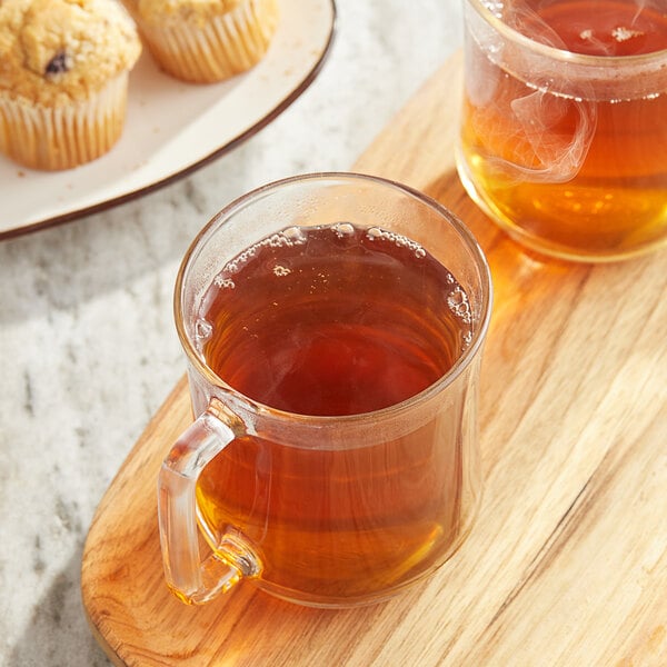 A wooden board with two glass mugs of Twinings Earl Grey Decaffeinated Tea and muffins.