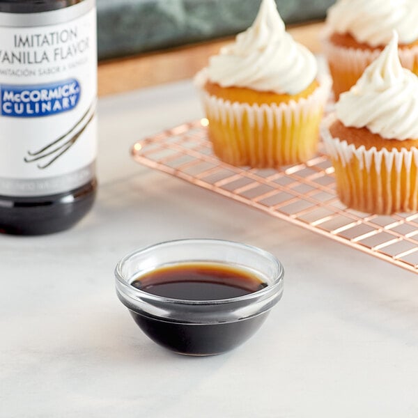 A cupcake with white frosting next to a bowl of McCormick Culinary Imitation Vanilla extract.