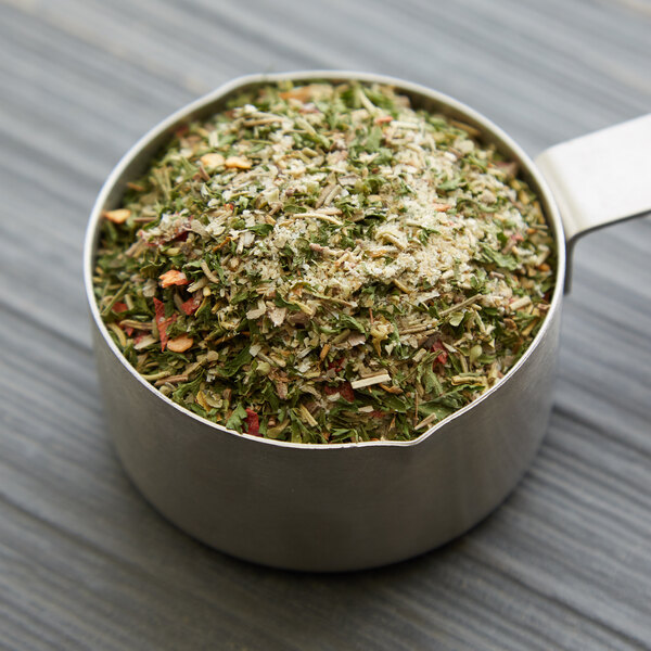 A metal measuring cup with a mixture of Regal Herbs & Garlic Blend.