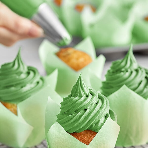 A hand using Chefmaster Leaf Green food coloring to frost a cupcake.