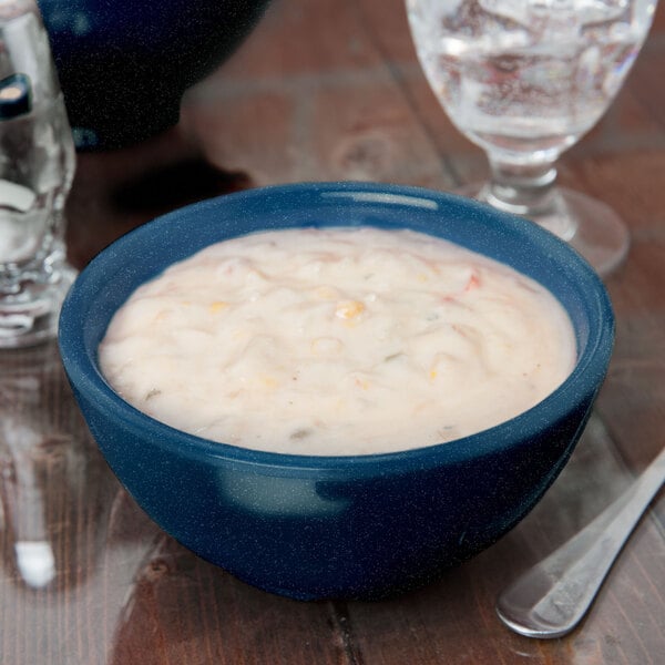 A Texas Blue melamine bowl of food on a table next to a glass of water and a plate.