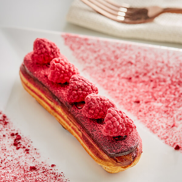 A dessert on a white plate with a spoon and freeze-dried raspberries on top.