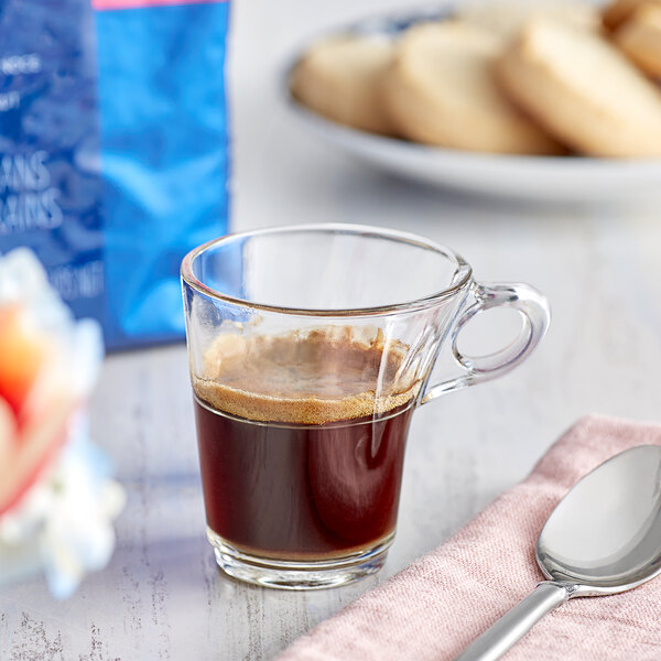 A glass cup of Lavazza whole bean espresso on a table with a spoon.