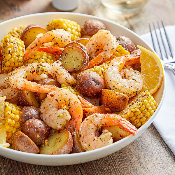 A bowl of shrimp, corn on the cob, and potatoes with spices.
