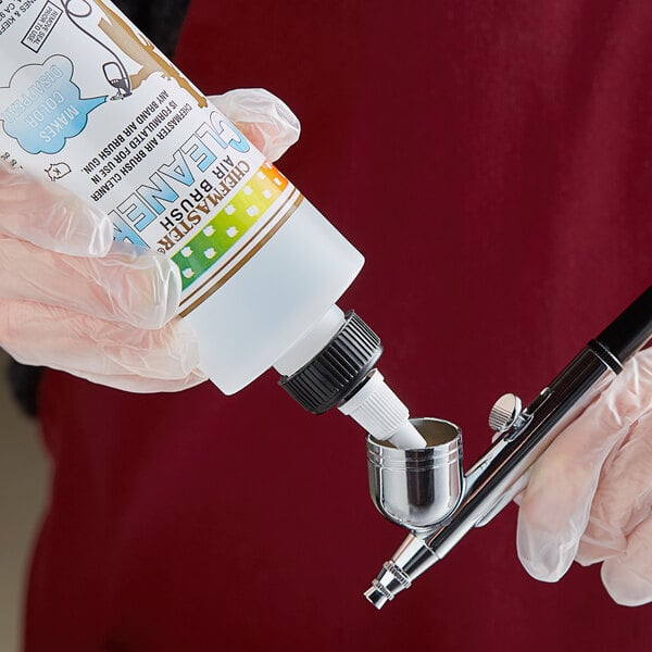 A hand in gloves holding a plastic bottle of Chefmaster Airbrush Cleaner.