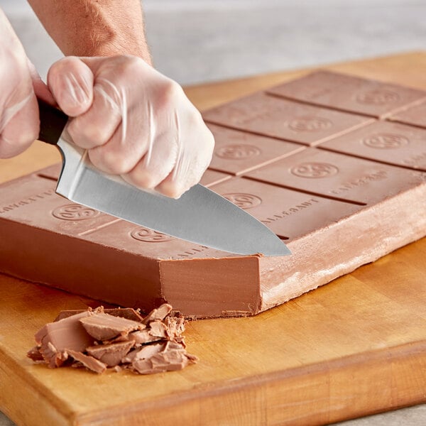 A person's hand using a knife to cut a Callebaut milk chocolate block.