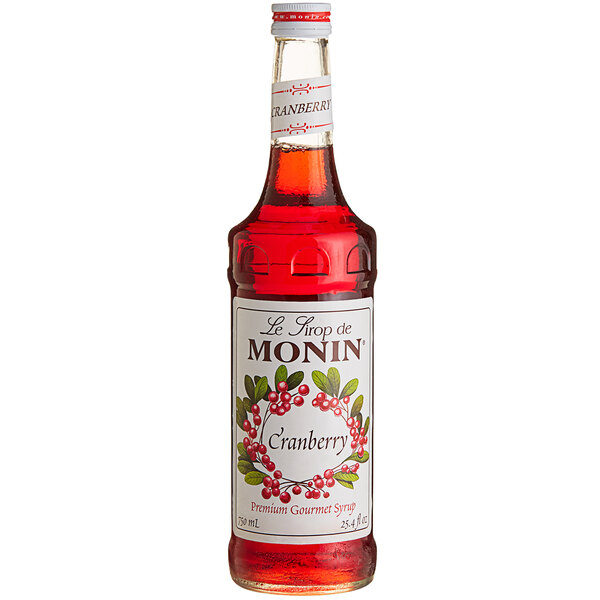 A close up of a bottle of Monin cranberry syrup with red liquid inside.