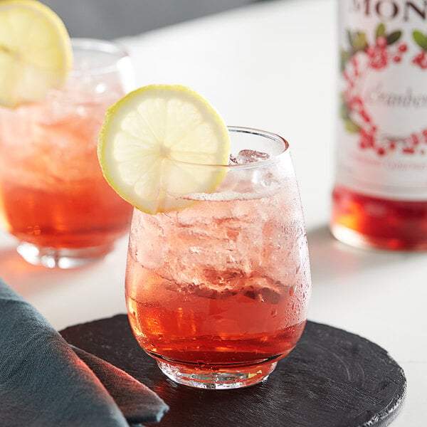 A glass of red liquid with a slice of lemon on top of it on a table in a cocktail bar.