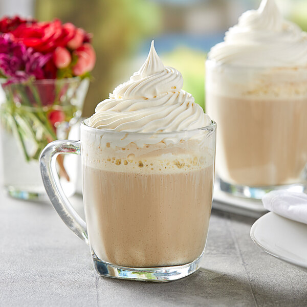 A glass mug of Capora vanilla latte/frappe mix with whipped cream on top.
