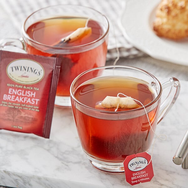 A glass cup of Twinings English Breakfast Tea with a tea bag in the background.