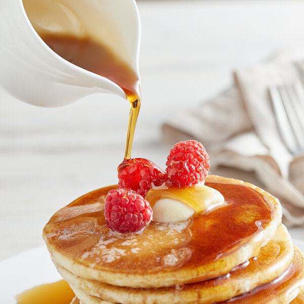 A stack of pancakes with Butternut Mountain Farm organic maple syrup and raspberries on a white plate.