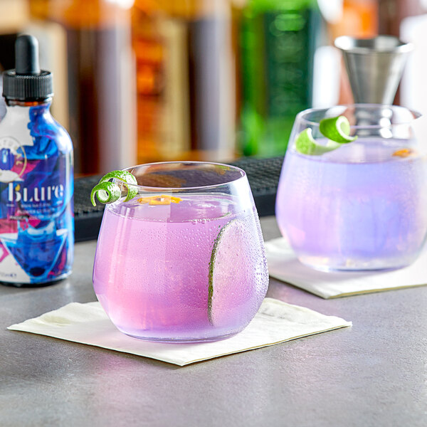 Two glasses of purple Wild Hibiscus floral extract with lime slices on a bar counter.