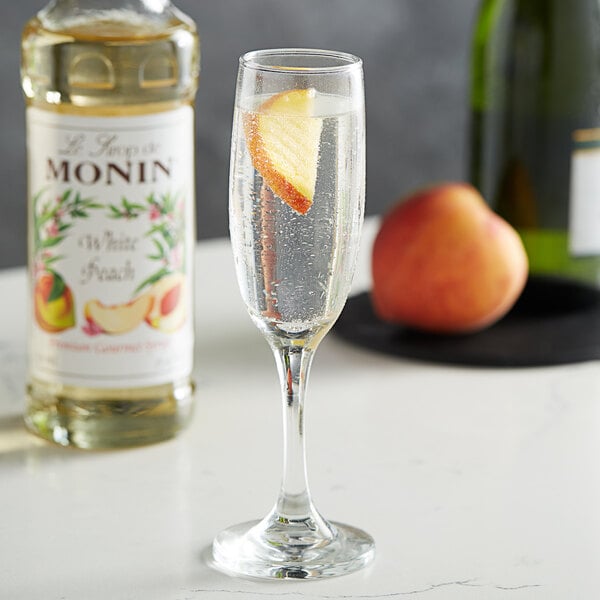 A glass of champagne with a Monin white peach flavoring syrup on a table.
