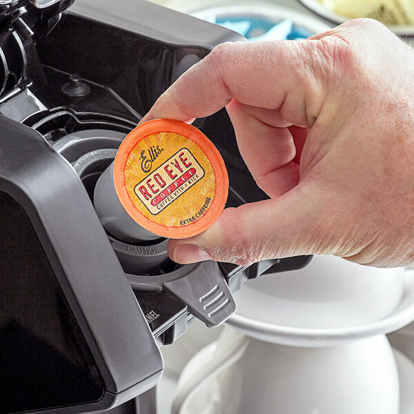 A hand holding a red Ellis single serve coffee cup with a grey lid.