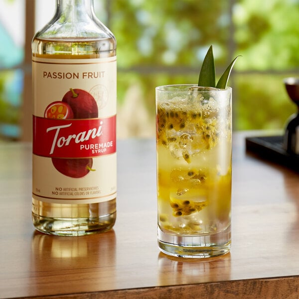 A glass of passion fruit juice next to a bottle of Torani Passion Fruit syrup.