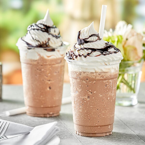 Two brown drinks made with Capora mocha frappe mix in plastic cups with whipped cream and chocolate syrup.