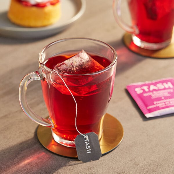 A glass mug of red Stash Wild Raspberry Hibiscus tea with a tea bag on the side.