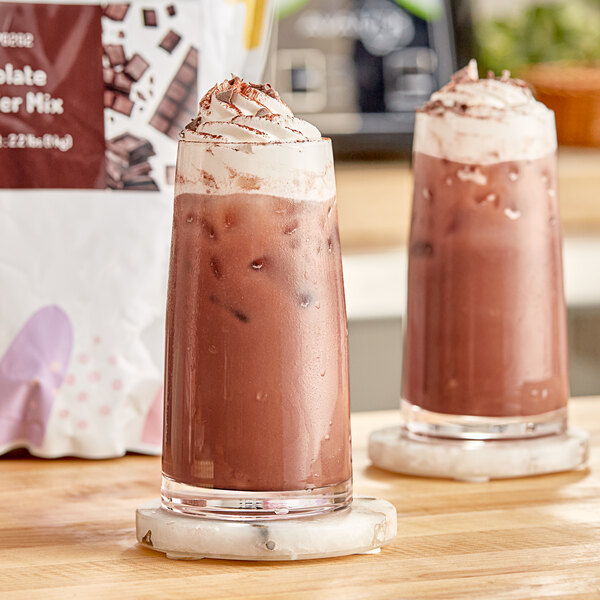 Two glasses of chocolate milk with whipped cream and chocolate chips made with Bossen Chocolate Powder.