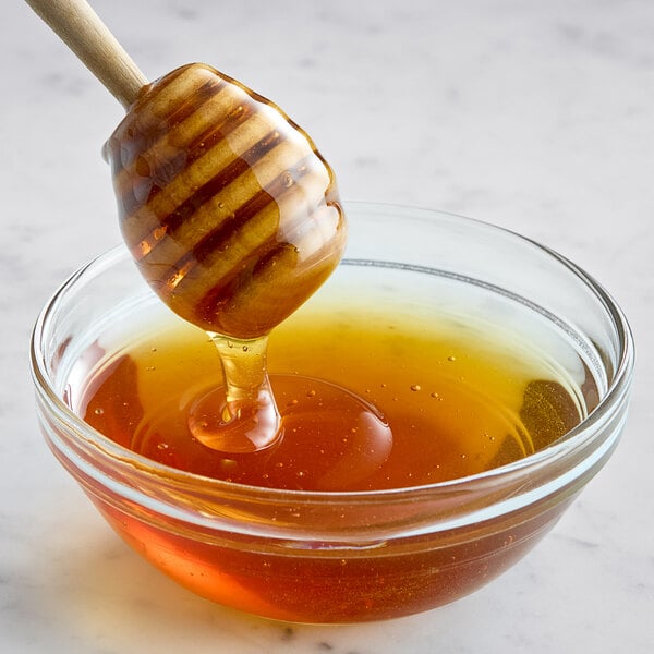 A honey dipper dripping honey into a bowl.