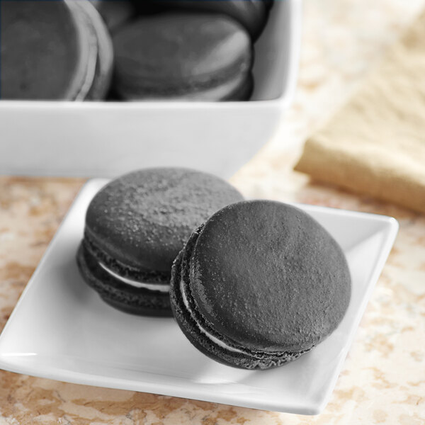 A white plate of black and white cookies with a Chefmaster Natural Black Liqua-Gel Food Coloring black cookie on it.