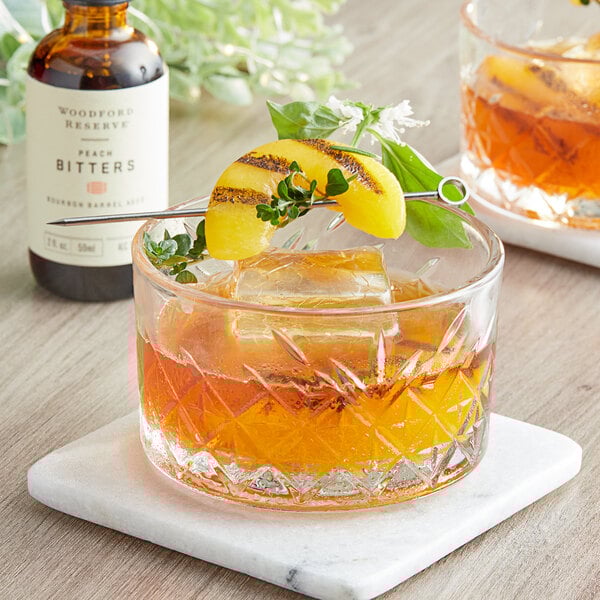 A glass of Woodford Reserve Peach Bitters in a cocktail with a slice of peach on top.