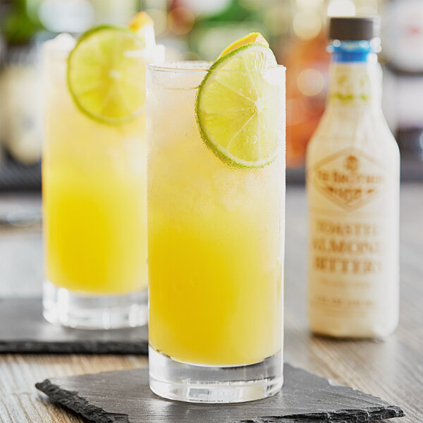 A glass of yellow liquid with a lime slice on the rim.