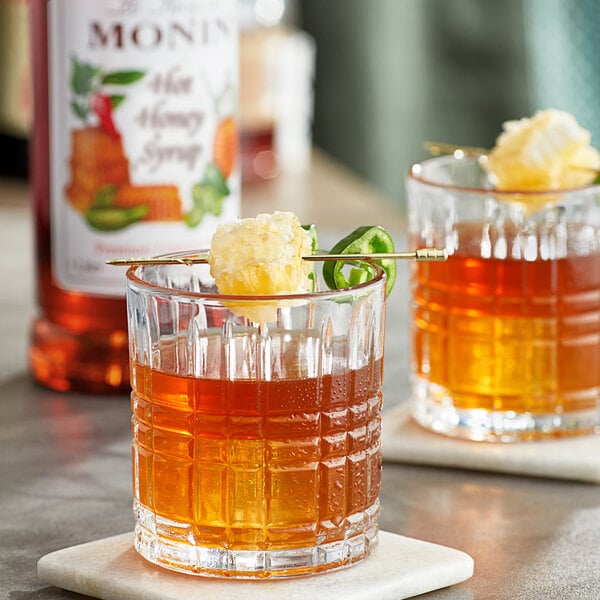 Two glasses of Monin hot honey whiskey on a table with a garnish stick.