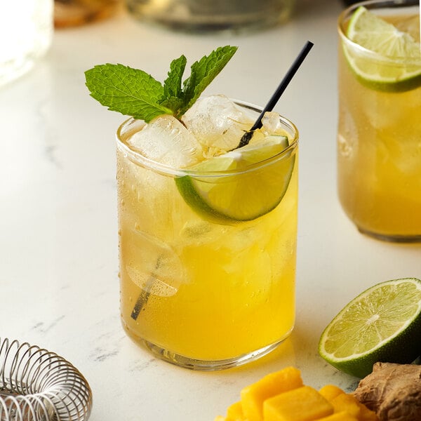 Two glasses of yellow drinks with lime and mint leaves on a table.