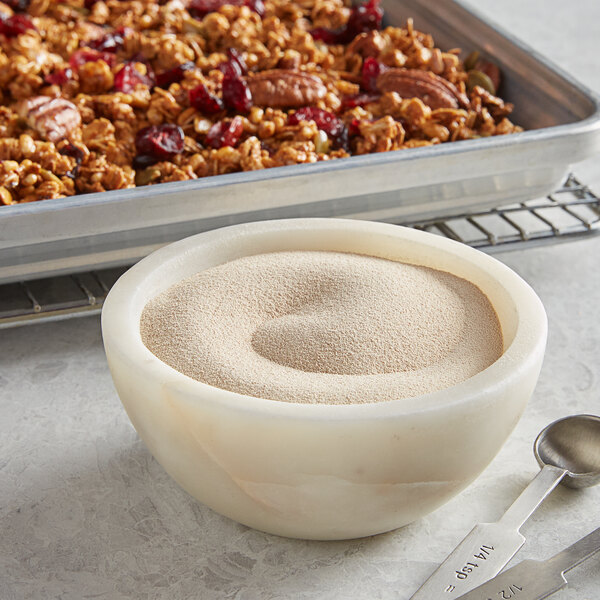 A bowl of granola with a measuring spoon of white powder on a table.