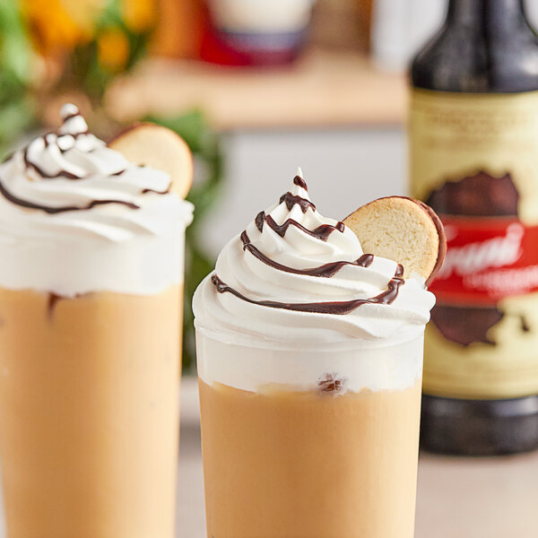 Two glasses of Torani Chocolate Milano flavored drinks with whipped cream and a cookie with chocolate drizzle on top.