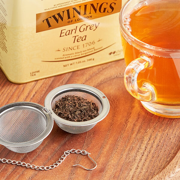 A strainer full of Twinings Earl Grey loose leaf tea over a glass mug of tea.