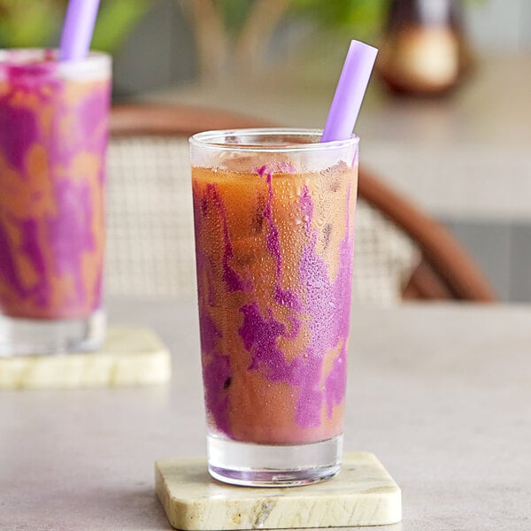 A glass of purple sweet potato bubble tea with a straw on a table.