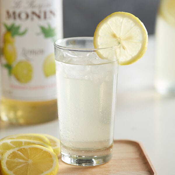 A glass of clear liquid with ice and a lemon slice in it.