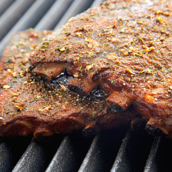 Regal Savory Grill Seasoning being used to season meat on a grill.