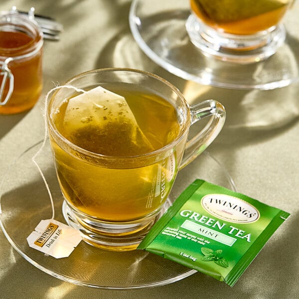 A glass mug of Twinings green tea with mint with a tea bag in it.