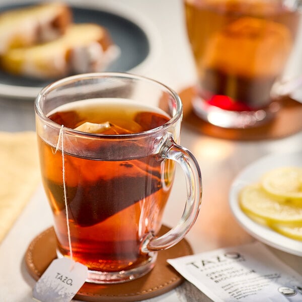 A glass mug of Tazo Organic Earl Grey Tea with a tea bag in it on a table with food.